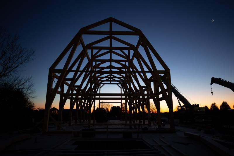 The gambrel timber frame awaits the arrival of the crew in the early pre-dawn light • Crane stands by ready