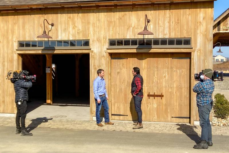 Camera crew focuses their lenses on Everett & Jonathan in front of The Barn Yard’s Carriage Barn