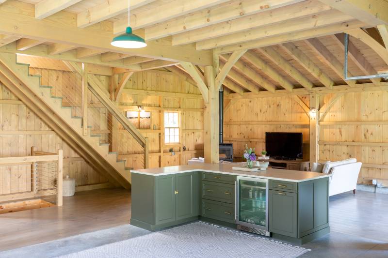 Classy kitchen cabinets, a beverage fridge, and quartz countertop in a large gathering space with pendant lighting & timbers overhead