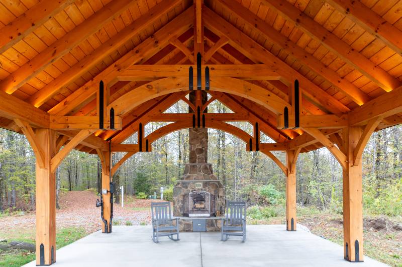 Stone fireplace and two rocking chairs beneath the timber frame pavilion