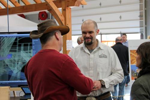 Design Manager Jim shares his excitement for timber framing with a visitor. A timber frame model is displayed on the monitor behind him.
