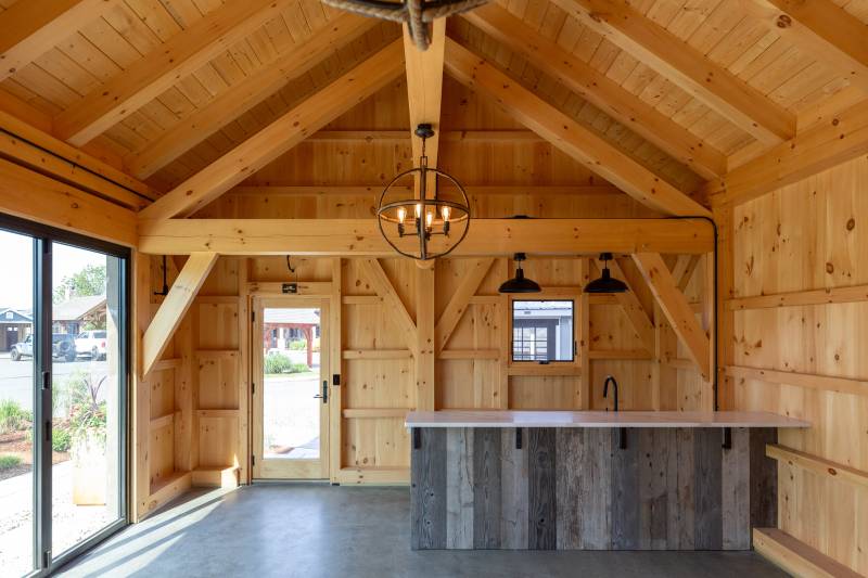 The left side of the timber frame pool house has an entry door and bar